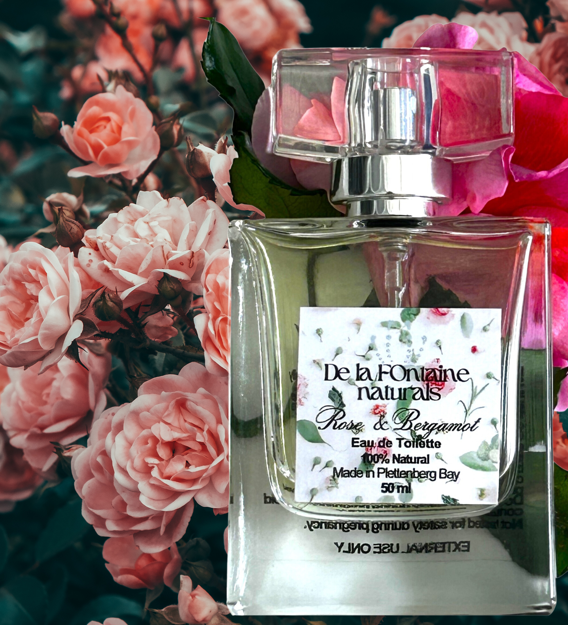 A clear glass bottle of De La Fontaine Rose & Bergamot Eau de Toilette with a white label, cap, and pink floral background.