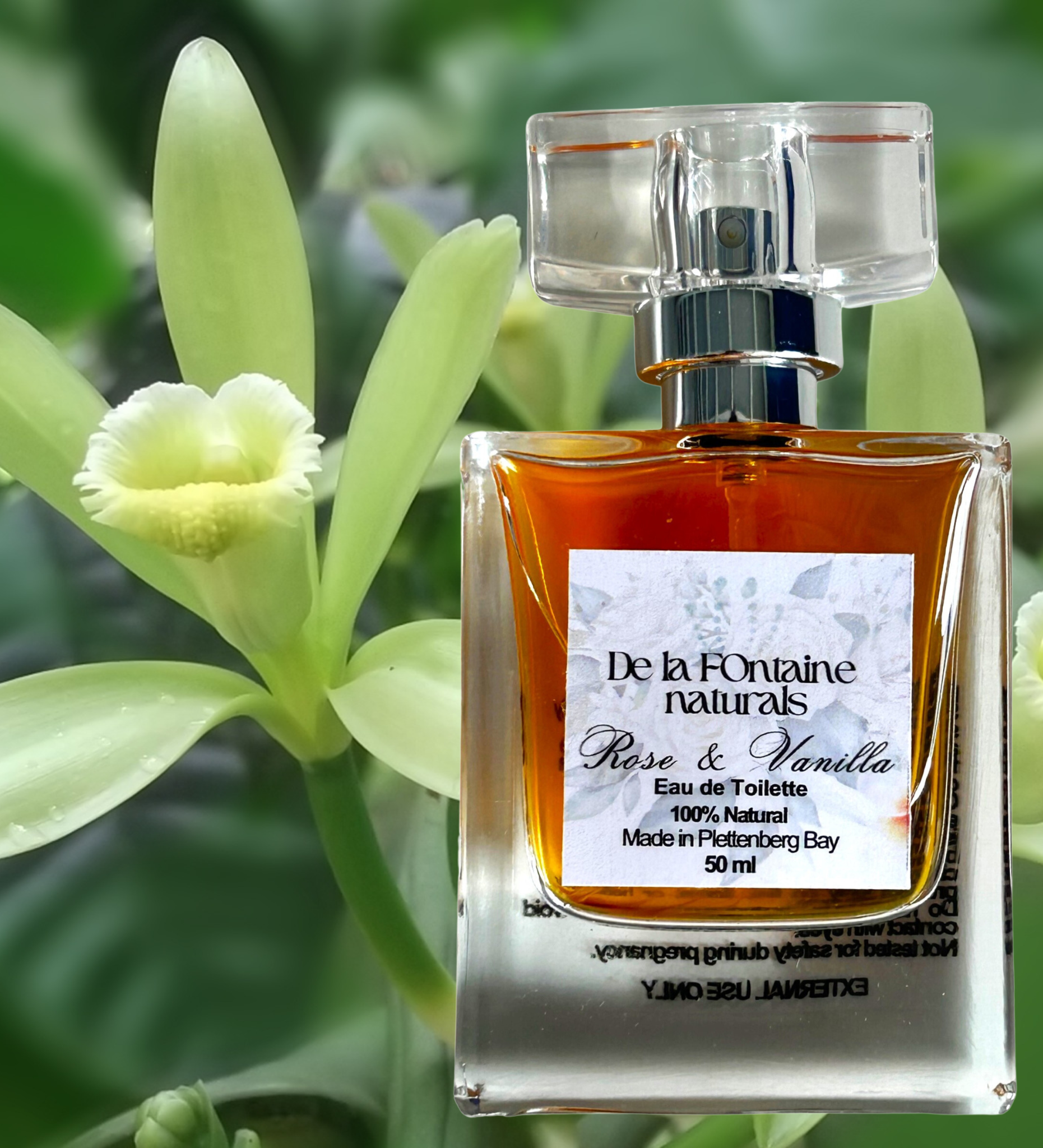 A bottle of De La Fontaine Rose & Vanilla Eau de Toilette with a clear liquid visible inside, placed on a table with a flower in the foreground.
